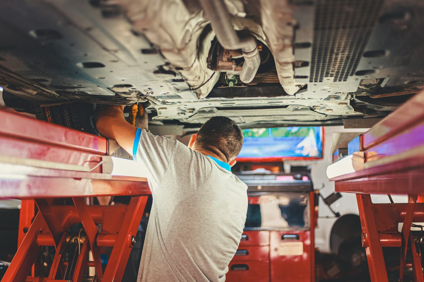 Mechaniker prüft die Unterseite eines aufgebockten Fahrzeugs in einer Werkstatt